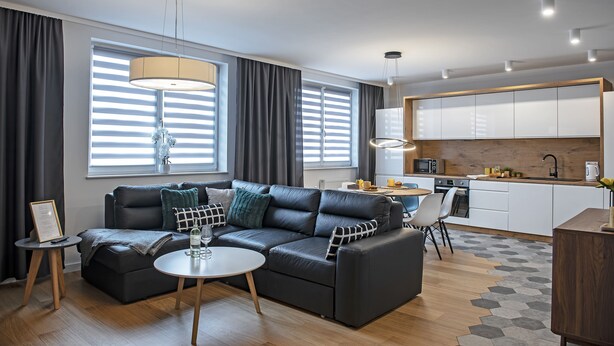 Un salon moderne avec un canapé, une table basse et un coin repas, la cuisine étant visible au fond.