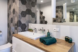 Bathroom features a large sink, geometric tile wall, and a mirror above.