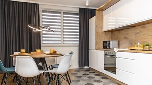 Une cuisine moderne avec des armoires blanches, un four à micro-ondes et un plan de travail en bois. On y trouve une table à manger avec des chaises et un luminaire suspendu.