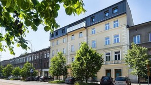 Une rangée d’immeubles résidentiels à plusieurs étages, dotés de balcons, avec des voitures garées et des arbres le long de la rue.