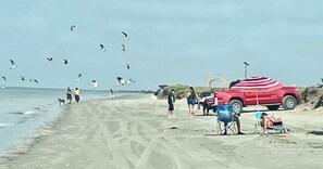 A beach scene with a red vehicle, a blue chair, and people walking.