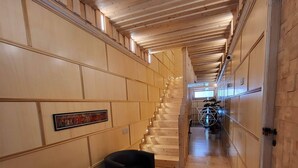 Un interno in legno con una scala che conduce a un piano superiore, una poltrona nera e un tavolino con un oggetto decorativo.