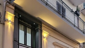 Facciata di un edificio con un'ampia entrata, un balcone con ringhiera in ferro battuto e una finestra con grate.