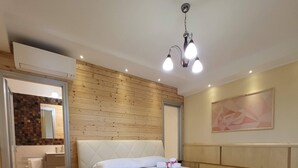 Una camera d'albergo con pavimento in legno, un letto con lenzuola bianche, un tavolino rotondo, uno specchio e un quadro appeso al muro.