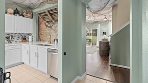 Une cuisine avec des meubles blancs, une fresque murale représentant une carte et un tonneau en bois dans le couloir.