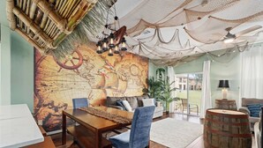 Un espace repas comprenant une table en bois, des chaises, une fresque murale représentant une carte et un luminaire suspendu.