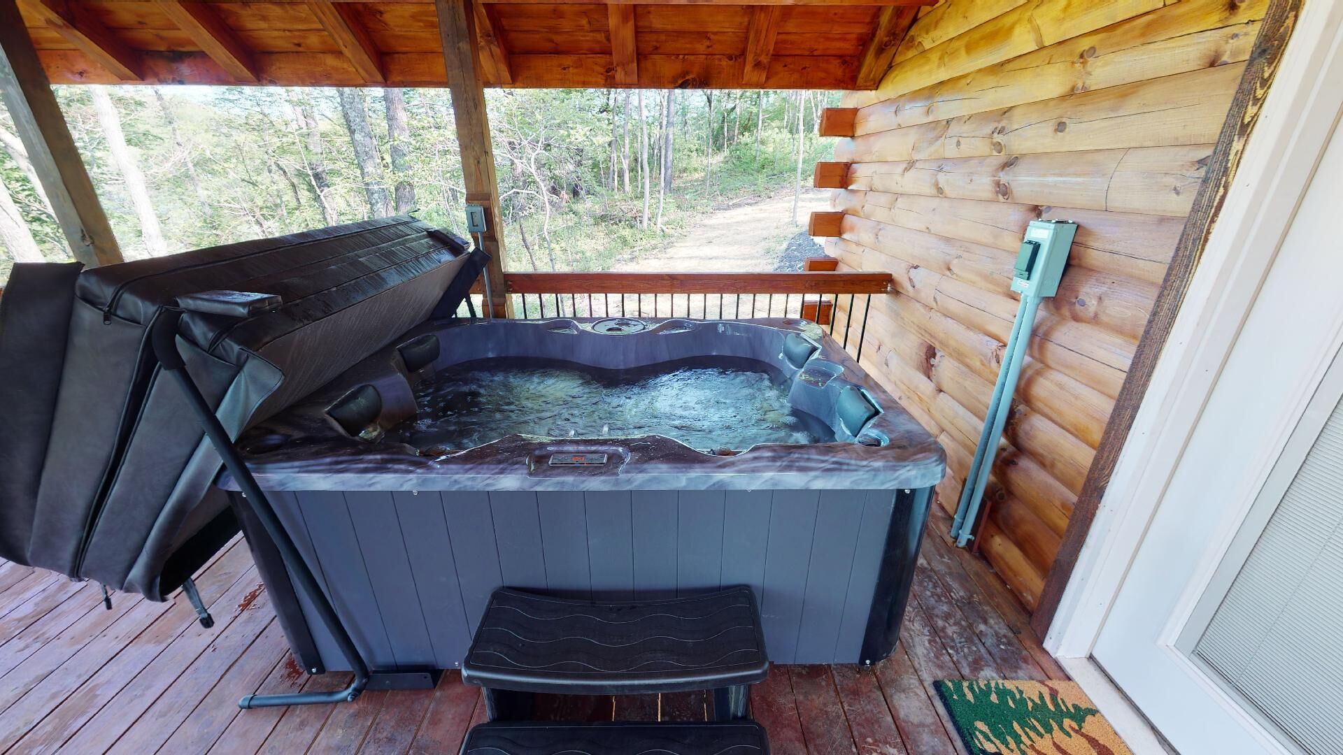 Un jacuzzi en una terraza de madera, con una cabaña de madera al fondo.