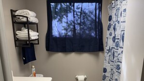 Ein kleines Badezimmer mit Toilette, Waschbecken und einem Fenster mit Blick auf Bäume.
