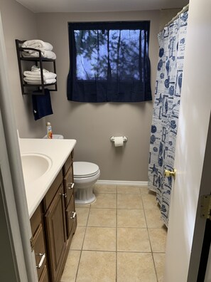 A small bathroom with a toilet, sink, and a window with a view of trees.