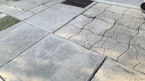 Ein überdachter Patio-Bereich mit Steinboden, Willkommensmatte, Topfpflanzen, Gartenmöbeln und einer Tür.