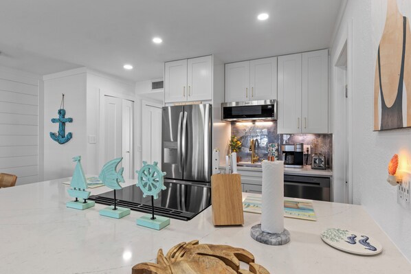 A modern kitchen with white cabinetry, stainless steel appliances, and nautical-themed decor. - Close to beach, private heated pool, bikes, beach chairs & more! (Holmes Beach)