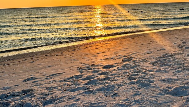 Une plage au coucher du soleil, avec le soleil se reflétant sur l’eau.