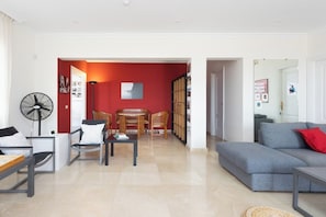 Un salon comprenant un canapé, des fauteuils, une table basse, un ventilateur et un mur d’accent de couleur rouge.