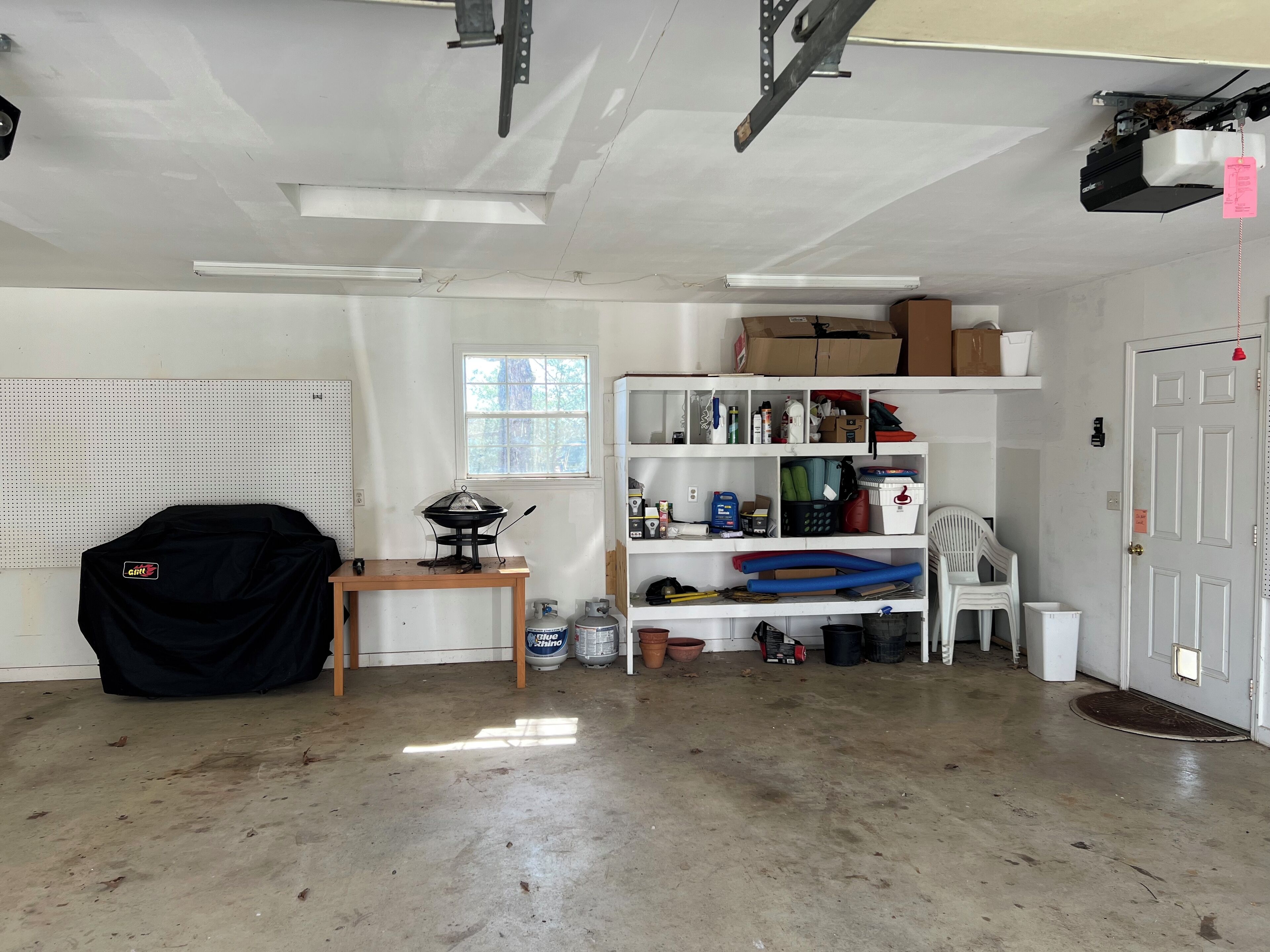 A garage with a workbench, shelves with various items, and a covered object on the floor.