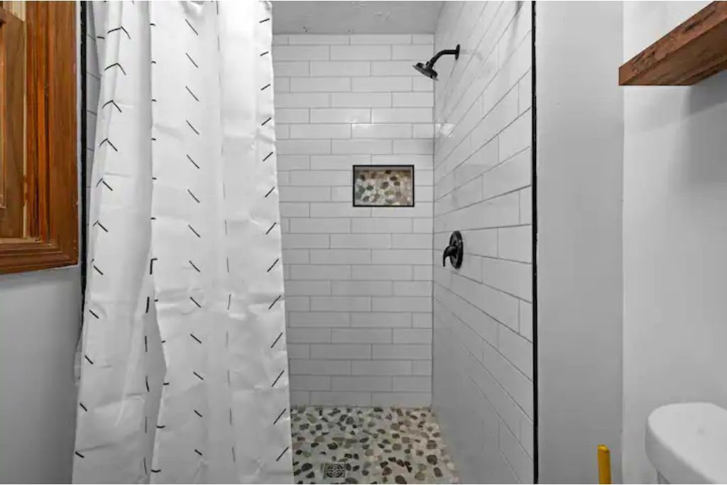 Un área de ducha pequeña y cerrada, con paredes de azulejos blancos y un cabezal de ducha.
