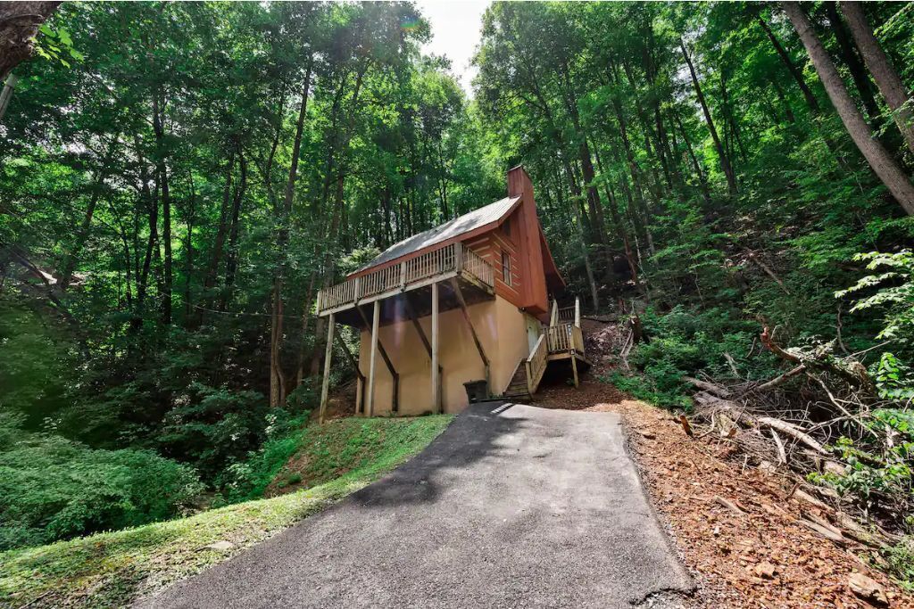 A wooden cabin with a balcony, surrounded by dense forest.