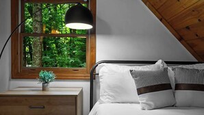 A bedroom with a wooden headboard, a nightstand with drawers, a bedside lamp, and a window with a view of greenery. - Romantic Smoky MTN Cabin • Hot Tub • Creekside • Near Dollywood • 1mi 2Pkwy (Sevierville)