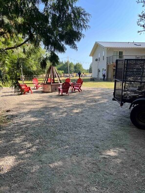 A gravel patio with red Adirondack chairs, a fire pit, and a metal grill.