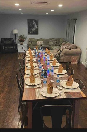 A dining table set for a meal with chairs, a sofa, a lamp, and a painting on the wall.