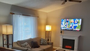 Ein Wohnzimmer mit einer Couch, einem an der Wand montierten Fernseher, einem Kamin und einem Deckenventilator.