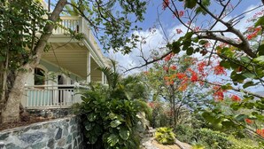 Uma casa com um caminho de pedra que leva a um alpendre, cercada por vegetação exuberante e plantas floridas.