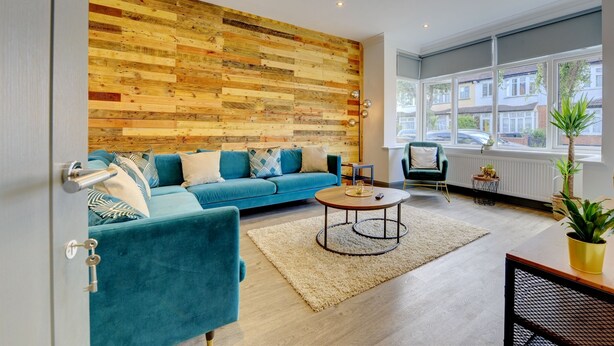 A modern living room with a blue sofa, a round coffee table, and a wooden wall panel. - The Cedars,family,contractors, Close to London B (Croydon)