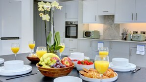 A breakfast setting with a variety of fruits, croissants, and orange juice on a table in a modern kitchen with white cabinets and appliances. - The Cedars,family,contractors, Close to London B (Croydon)