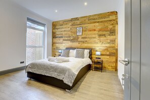 A bedroom with a wooden wall panel, a bed with white bedding, a nightstand, and a window with blinds. - The Cedars,family,contractors, Close to London B (Croydon)
