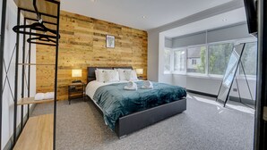 A modern bedroom with a wooden wall, a large bed, a bedside table, and a window. - The Cedars,family,contractors, Close to London B (Croydon)