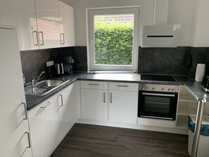 Cozinha moderna com armários brancos, bancada preta, forno embutido e janela com vista para áreas verdes.