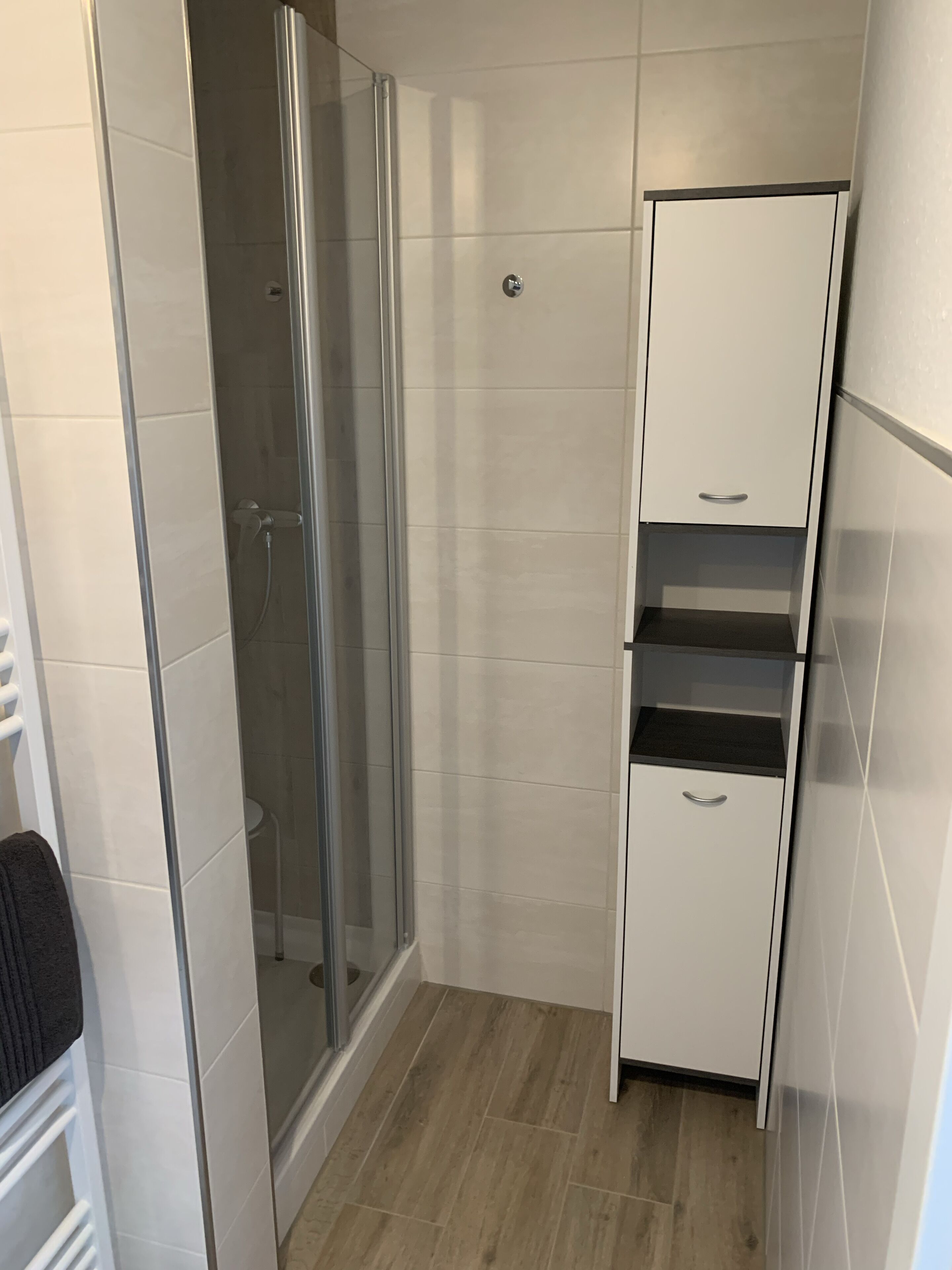 Un baño pequeño con mampara de vidrio, un mueble blanco con varios cajones y un perchero para toallas.
