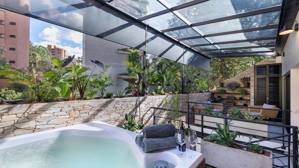 Um jardim no terraço com hidromassagem, paredes de pedra e vasos de plantas.