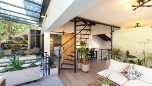 Ampla sala de estar com escada, piso de madeira e plantas em vasos.