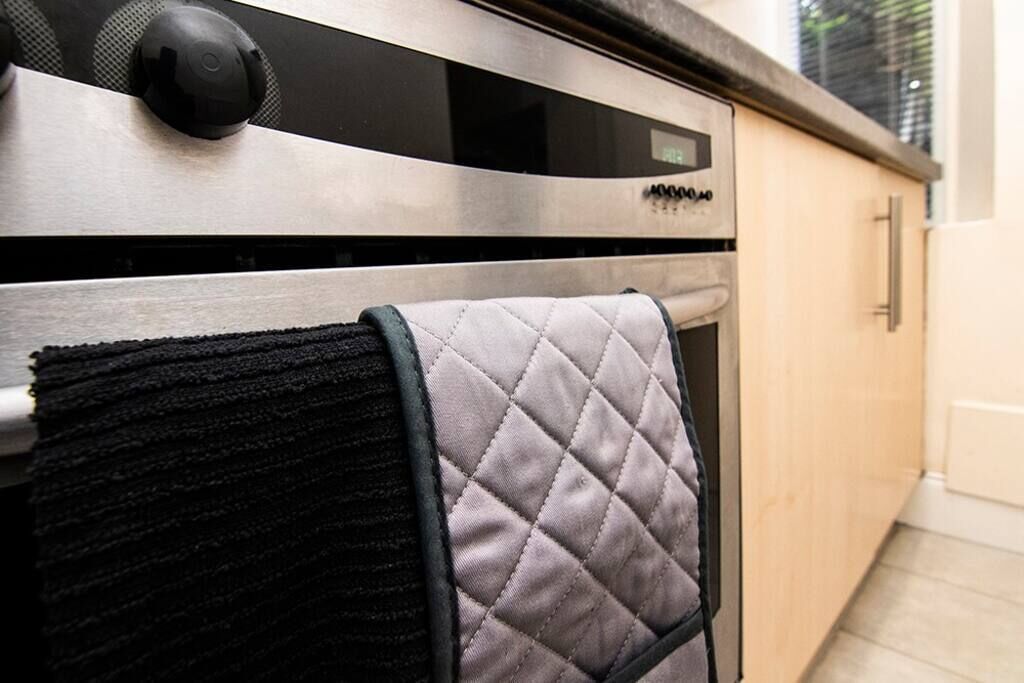 Een keuken met een roestvrijstalen oven, een zwart-wit geblokte handdoek aan een rek, en houten kastjes.