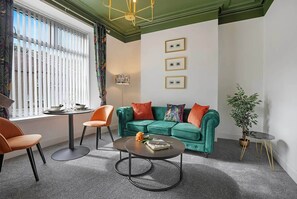 Una sala de estar moderna con un sofá verde, sillones naranjas, una mesa de centro redonda y una planta en maceta.