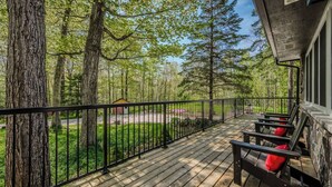 A wooden deck with a railing, surrounded by trees and a small building in the background.