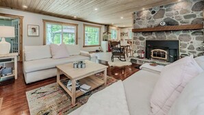A cozy living room with a stone fireplace, wooden ceiling, and large windows.