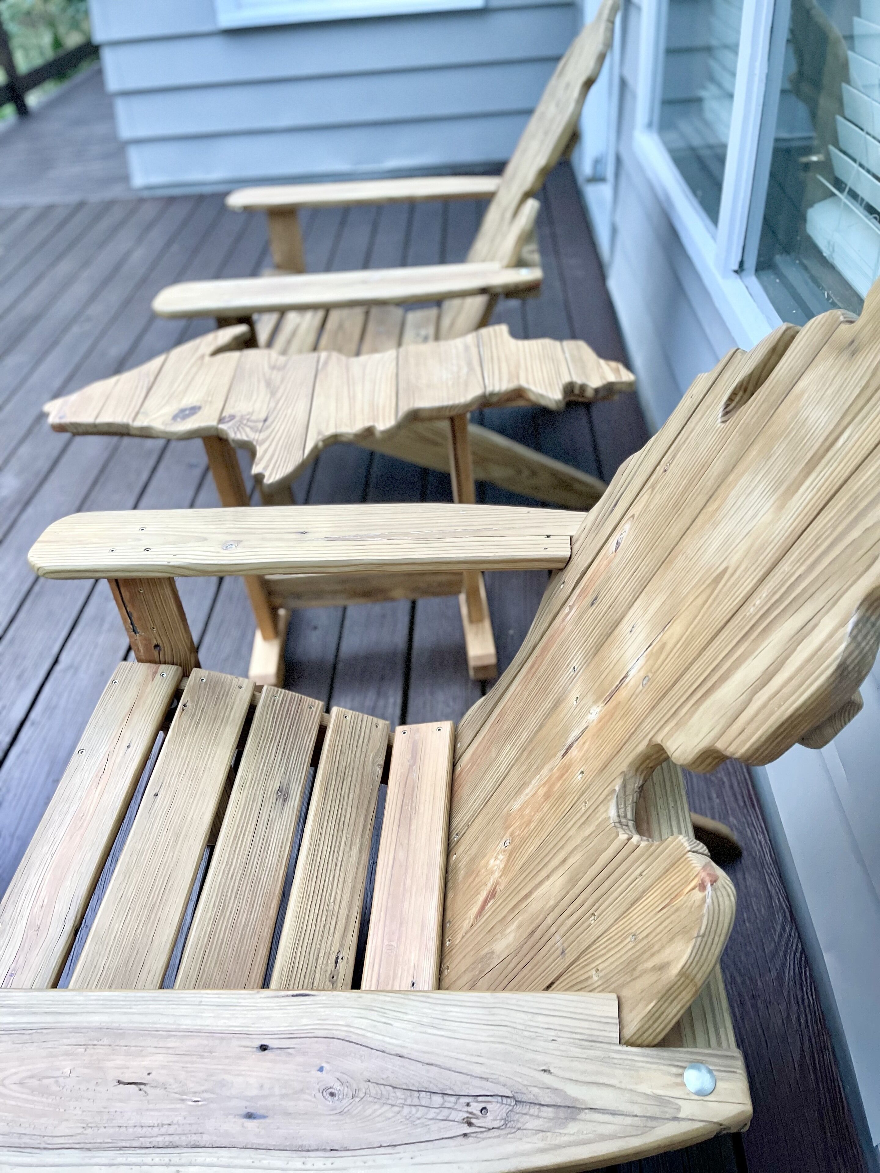 A wooden deck with three Adirondack chairs.