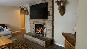 Una sala de estar con chimenea de piedra, televisor montado y cornamentas de ciervo en la pared.