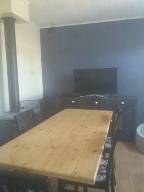 A dining area with a wooden table and chairs, a television on a stand, and a large pillar.