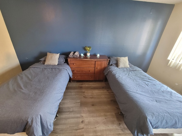 Une chambre à coucher avec deux lits simples, une commode en bois et un mur bleu.