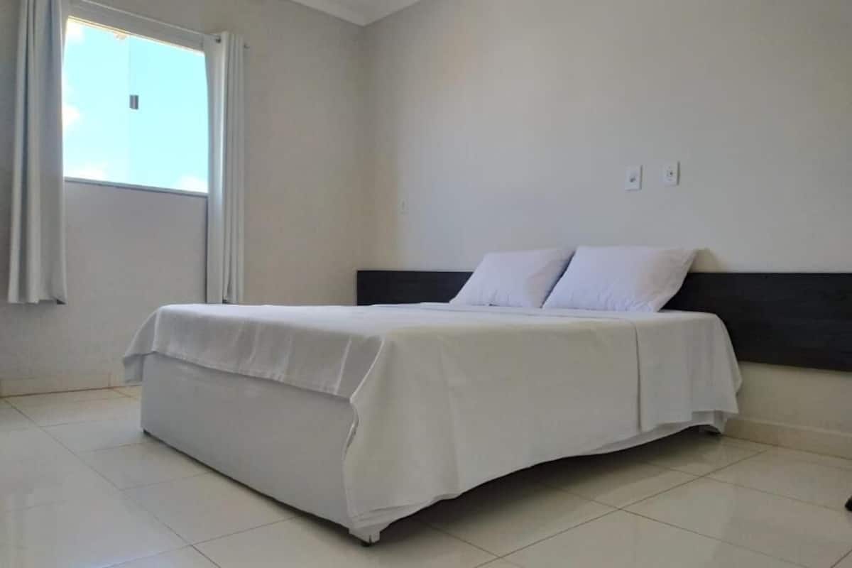 A clean, modern bedroom with a single bed, white bedding, and a window with curtains.