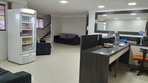 Un espacio de oficina moderno con un mostrador de recepción, un refrigerador lleno de bebidas, un sofá y una escalera que sube a otro nivel.