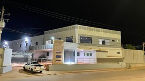Un edificio moderno de dos pisos con garaje, un coche blanco estacionado al frente y una entrada protegida por una reja.