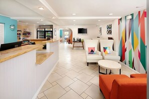 A modern hotel lobby with a reception desk, seating area with chairs and ottomans, a television, and a colorful wall mural. - Affordable Accommodation in Signature Temecula! Onsite Pool, Free Parking (Temecula)