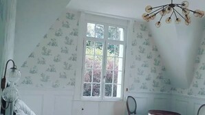 Un dormitorio con una cama grande, una ventana, una araña y una pequeña mesa con sillas.