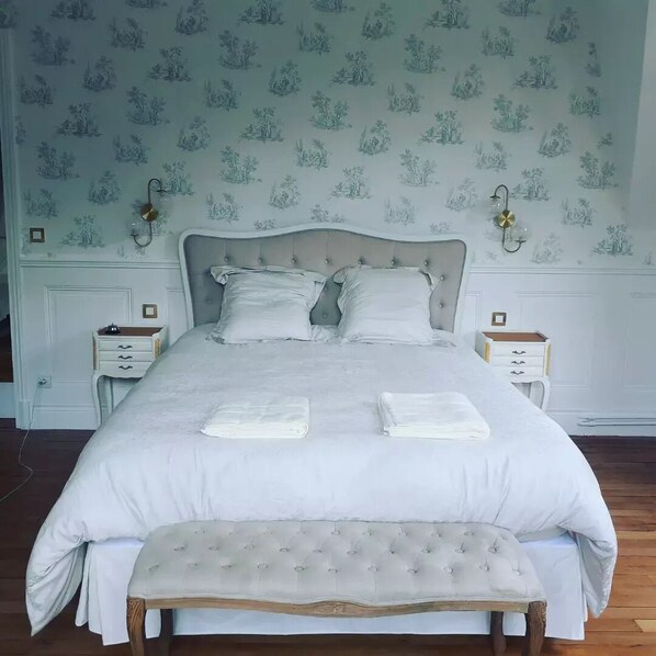 Una cama bien hecha con sábanas blancas, dos mesitas de noche con lámparas y un banco al pie de la cama.