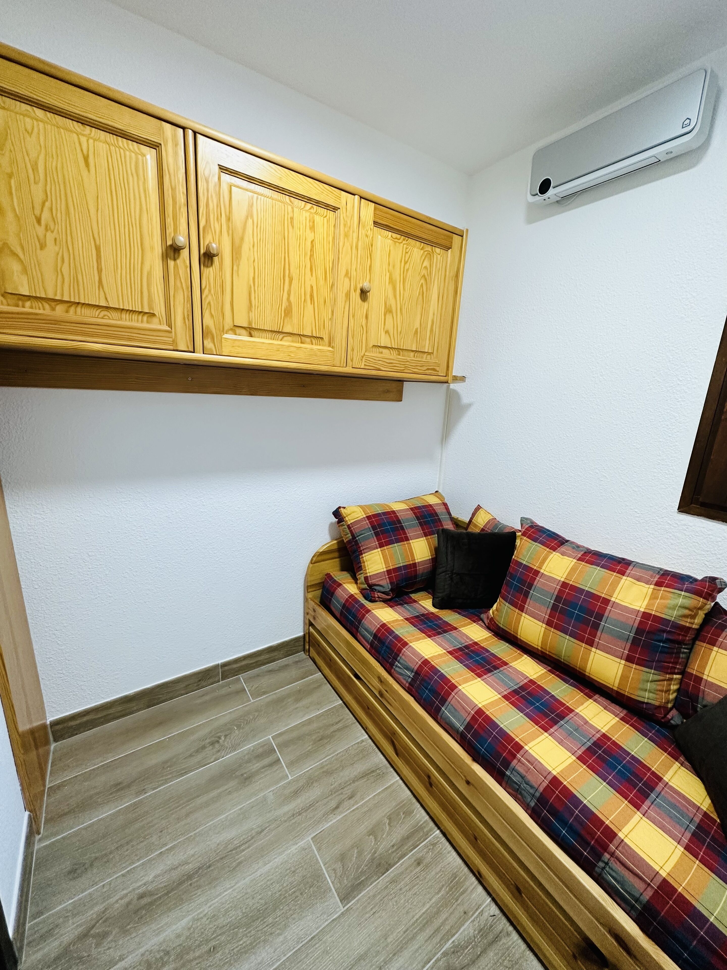 Une petite pièce avec un lit en bois, un mur blanc et une armoire en bois.