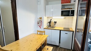 Cocina compacta con armarios blancos, microondas y un refrigerador pequeño. Hay una mesa de comedor de madera con cuatro sillas y dos taburetes.