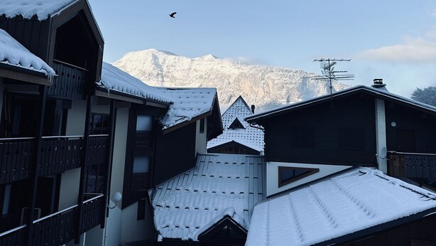 Un pueblo cubierto de nieve con edificios de madera tradicionales, cielo despejado y una montaña al fondo.